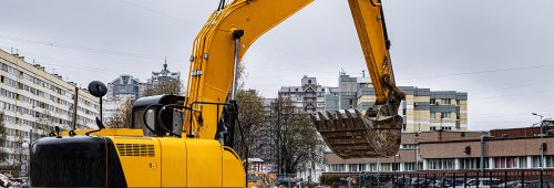 תמונת נושא של המאמר צו הריסה מנהלי המציגה מחפר צהוב גדול בשטח הריסה עם פסולת בנייה רבה ברקע בניינים ומפעלים ישנים.