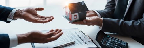 תמונת נושא של המאמר על עורך דין דיירים המציגה סצנת חתימה על עסקת נדל"ן. אדם בחליפה מגיש מודל של בית פרטי לאדם אחר. על השולחן הלבן מונח מסמך תחת הכותרת "CONTRACT AGREEMENT" עם עט, צרור מפתחות ומחשבון, המסמלים את השלב הסופי של רכישת נכס